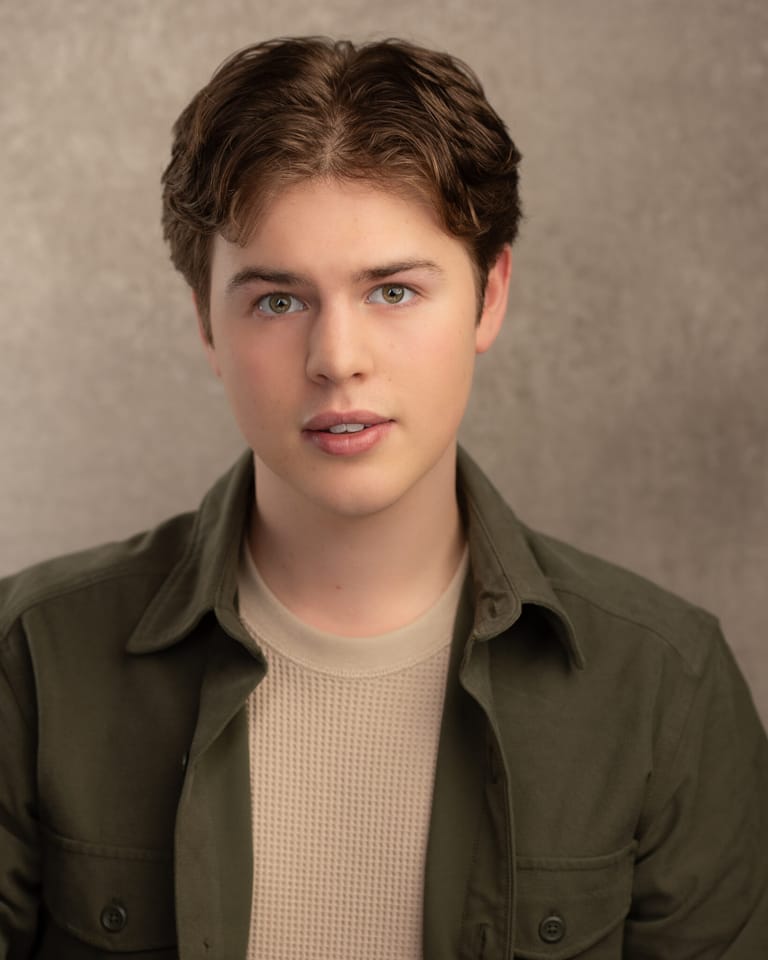 Young man in olive shirt and cream waffle-knit top against neutral grey background.