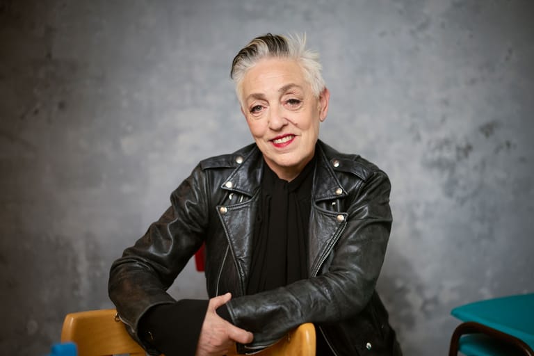 Person in black leather jacket seated against grey backdrop, smiling at camera.