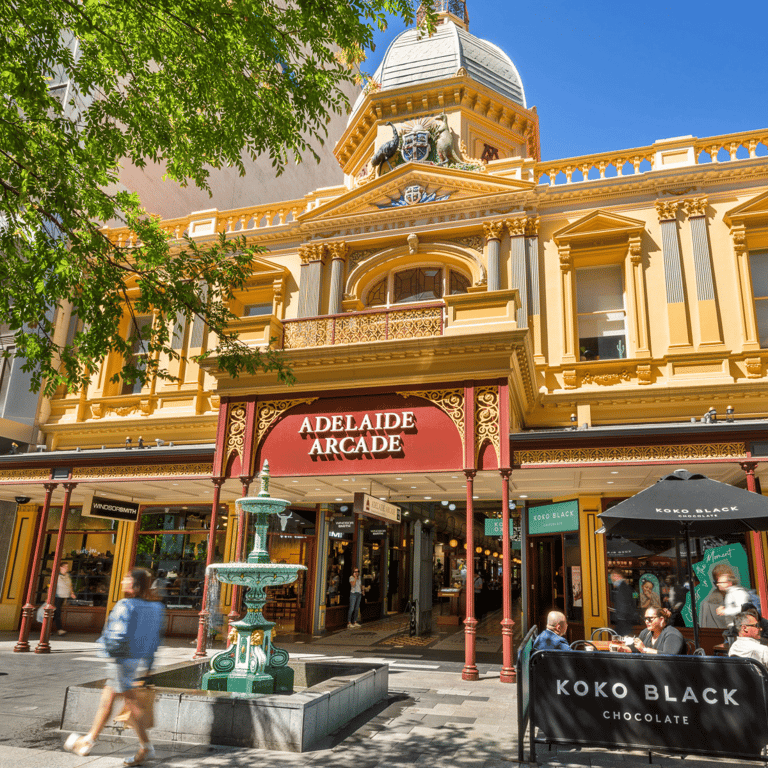 Historic Adelaide Arcade storefront with ornate golden Victorian architecture and red signage on a sunny day.