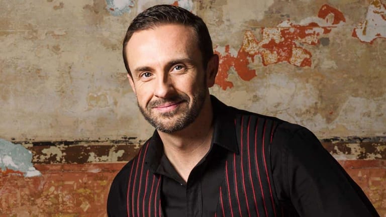 Man in black pinstriped shirt against a weathered, rust-stained concrete wall.