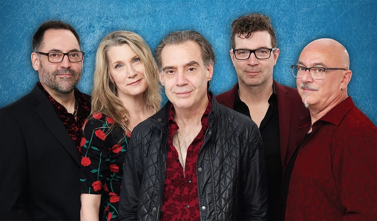 Five performers stand together against a blue backdrop in formal attire.