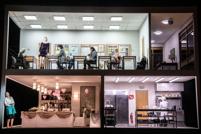 Window display divided into four illuminated sections showing theatre set designs and miniature stage scenes with furniture and props.