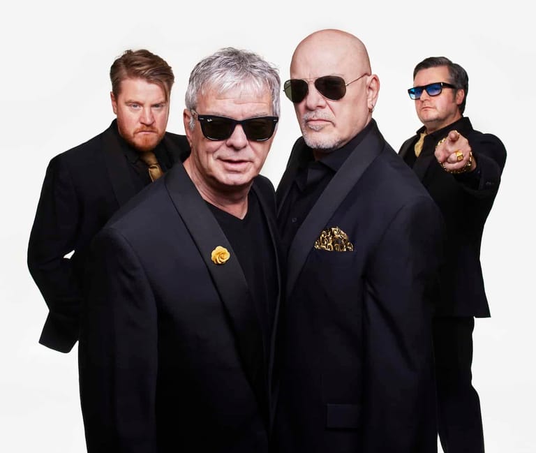 Four men in dark suits and sunglasses pose against a white background.