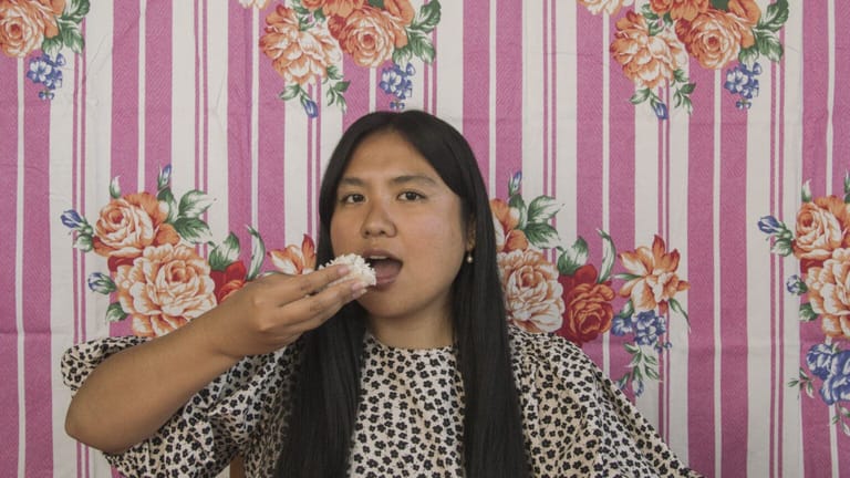 Woman in polka-dot top eating from her hand against a pink floral striped backdrop.