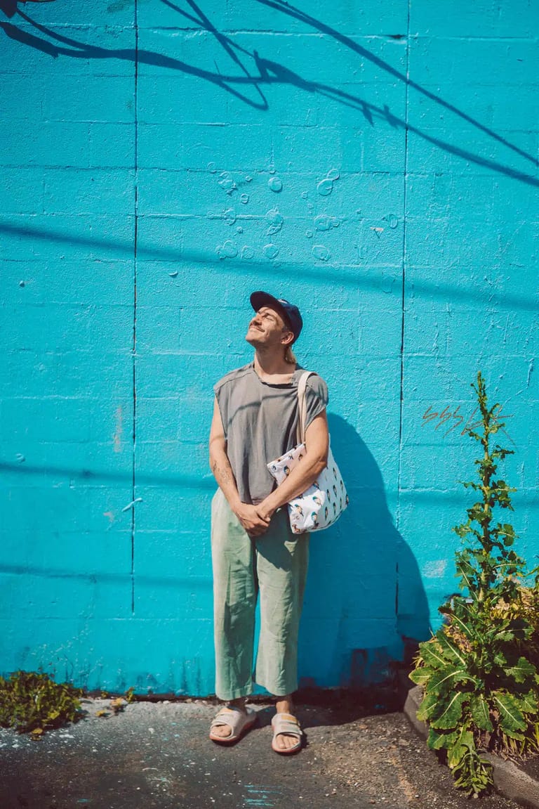 Person in casual wear standing against a bright turquoise wall casting sharp shadows.