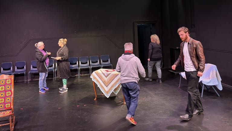 Children and adults interact during a participatory theatre performance on a dark stage with scattered props and seating.