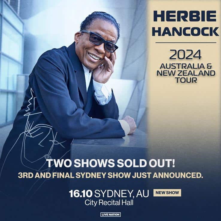 Man in dark suit and glasses smiles at camera in promotional image for Australia and New Zealand tour.