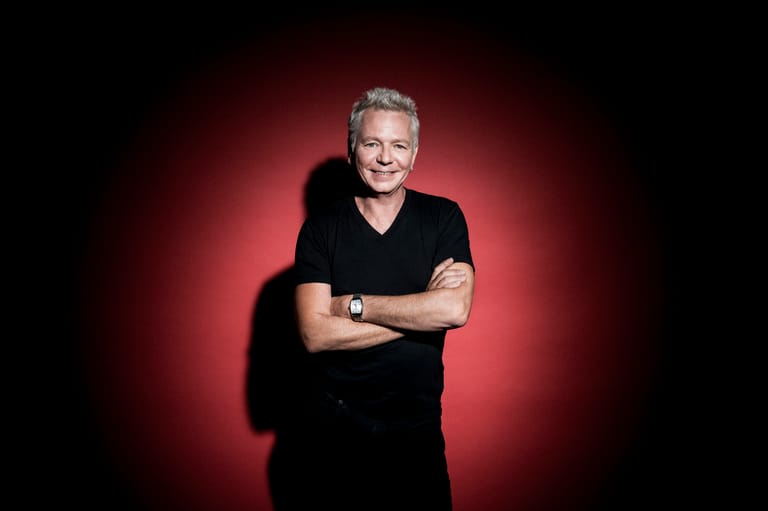 Person with arms crossed smiling at camera against a red gradient background.