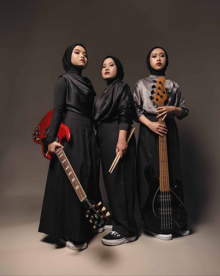Three musicians in dark robes hold electric guitars against a neutral grey backdrop, gazing upward.