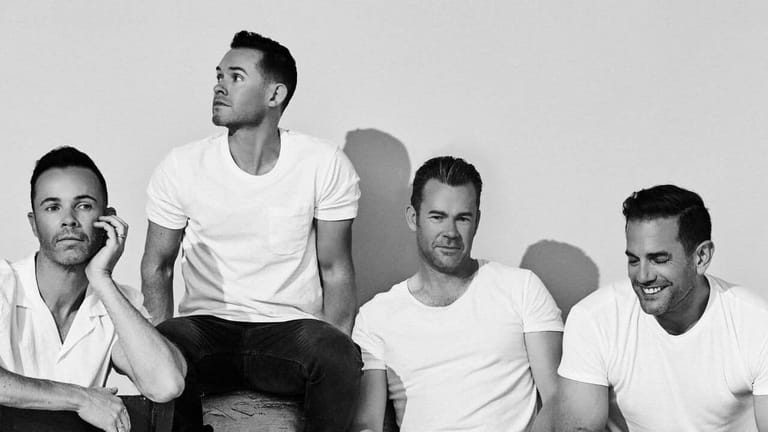 Four men in white shirts pose together against a neutral backdrop in black and white.