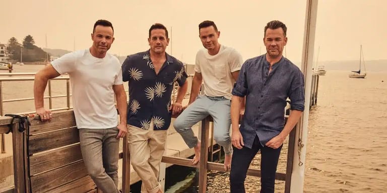 Four men posing on a wooden pier overlooking calm water at sunset or sunrise.
