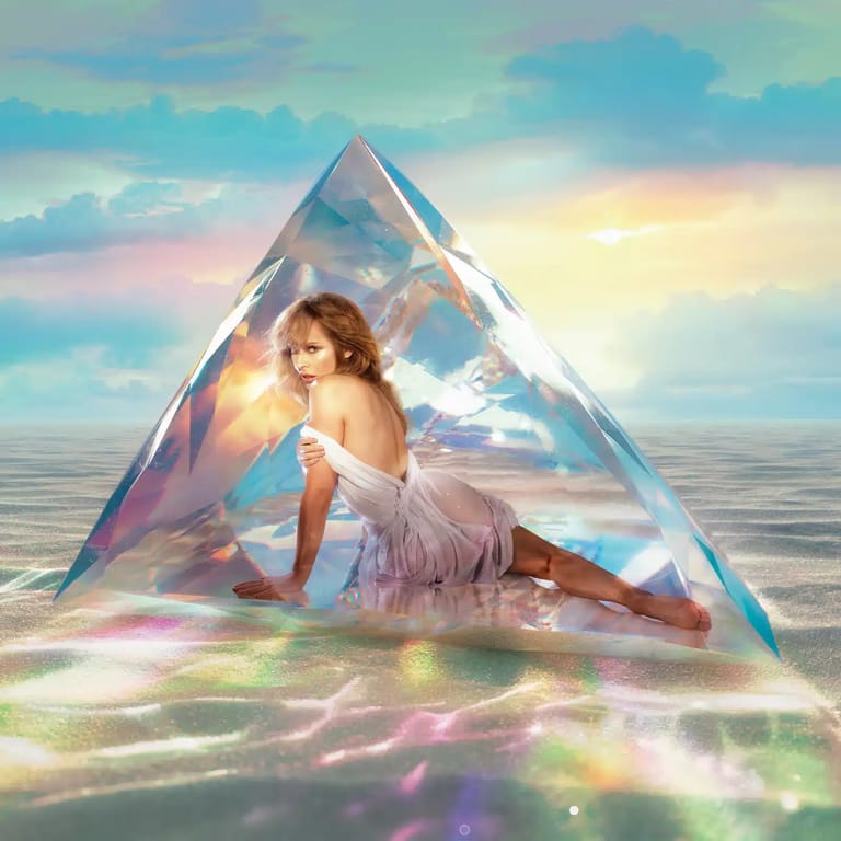 Person with microphone seated inside iridescent geometric tent amid colourful light patterns and cloudy sky backdrop.