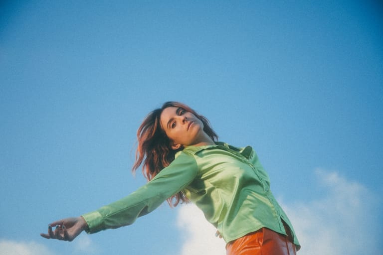 Person in lime-green jacket stretching arm against clear blue sky.