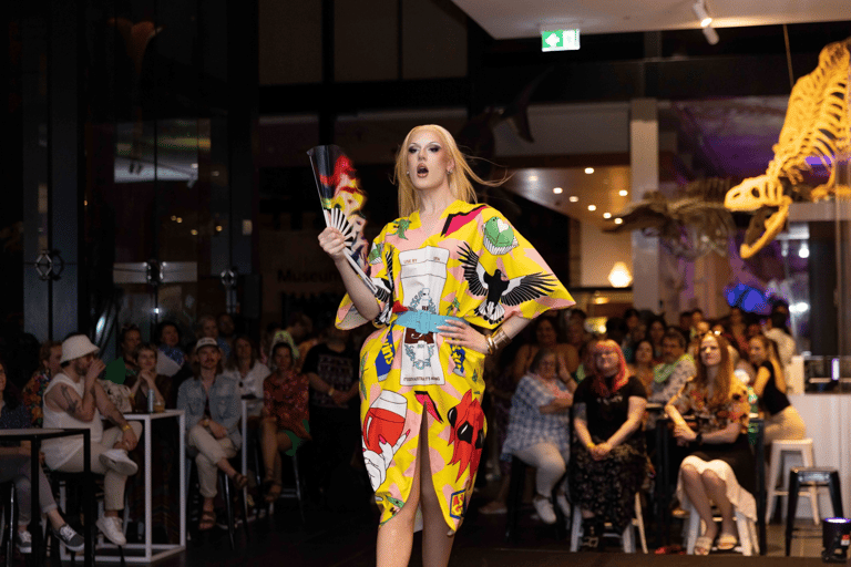Performer in vibrant yellow patterned outfit gestures to crowd during indoor stage event.