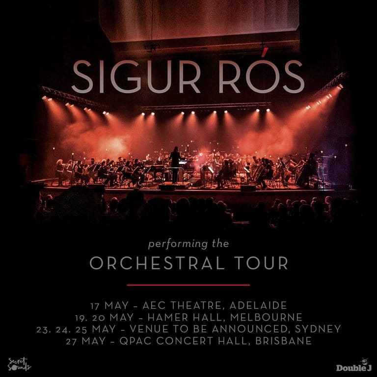 Sigur Rós performs with a full orchestra on stage bathed in warm orange lighting during their orchestral tour.