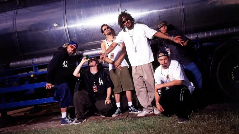 Group of six people posing together against a large metallic structure under purple stage lighting at night.