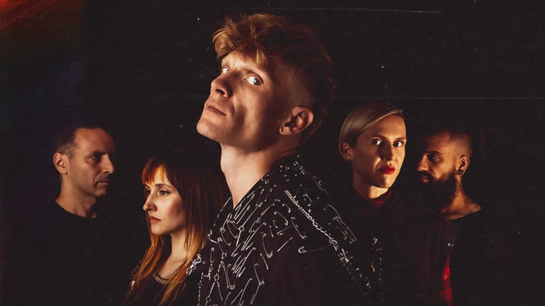 Five band members posed together in dramatic stage lighting against a dark background.