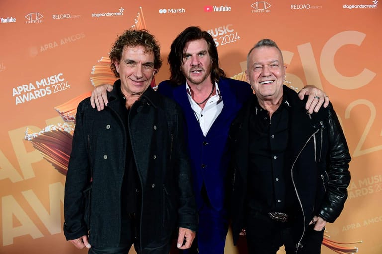 Three men pose together at an ARIA Music Awards event backdrop in formal black attire.
