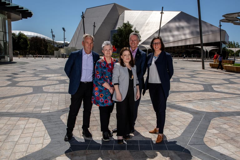 Five people stand together in a modern plaza with a contemporary building visible behind them.