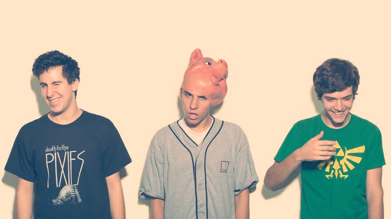 Three young men wearing band and graphic t-shirts against a cream background.