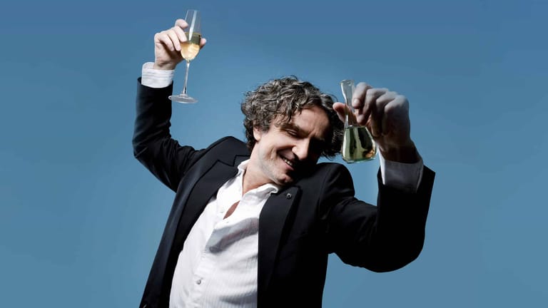 Man in black blazer and white shirt holds two awards aloft against a blue background.