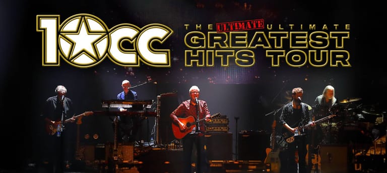10CC band members perform on stage during their Greatest Hits Tour under gold and red stage lighting.
