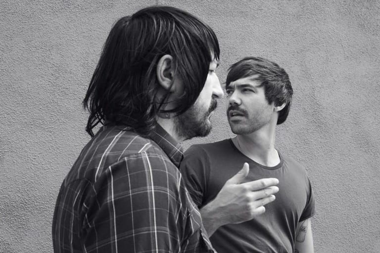 Two men in conversation against a plain wall, captured in black and white profile.