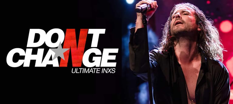 Long-haired performer in black shirt raises fist under stage lighting during Don't Change Ultimate INXS tribute show.