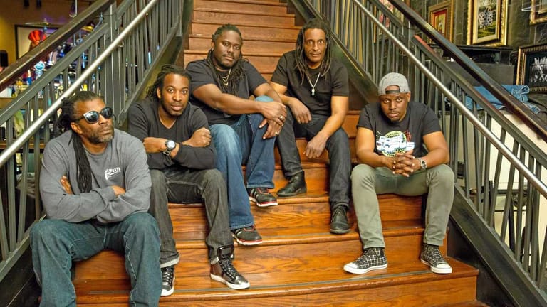 Five people seated together on wooden stairs in an indoor venue, wearing casual clothing and lanyards.