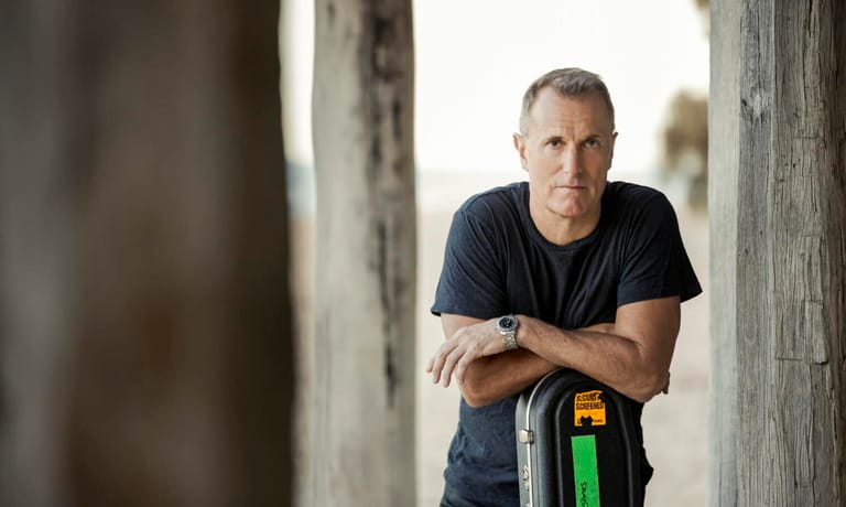 Man in dark shirt leaning against weathered concrete pillars in natural daylight.
