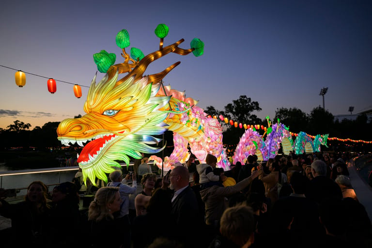 Illuminated dragon lantern glowing yellow and green above crowds at an evening festival celebration.