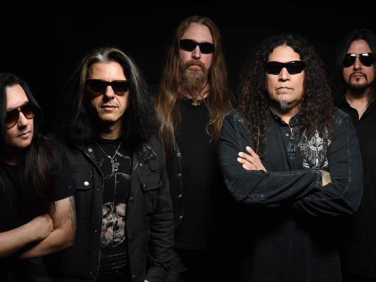 Five band members in sunglasses and dark clothing posed against a black background.