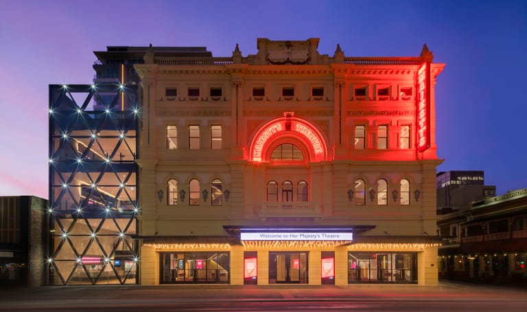 Historic theatre building illuminated with colourful neon lighting at dusk in an urban setting.
