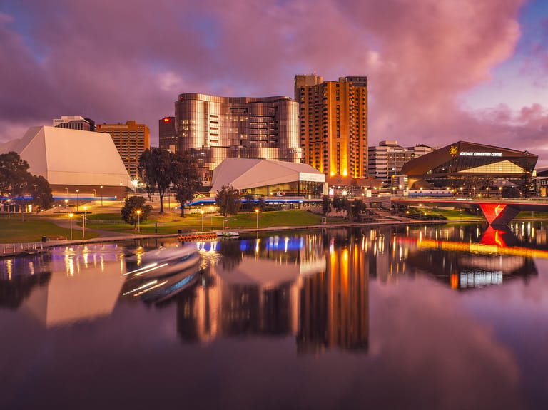Adelaide's cultural precinct at dusk with illuminated theatres and buildings reflected in the Torrens River.