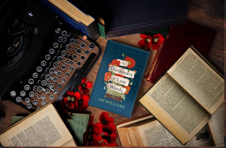 Vintage typewriter, open books, and red flowers arranged on a dark surface with a blue book cover.