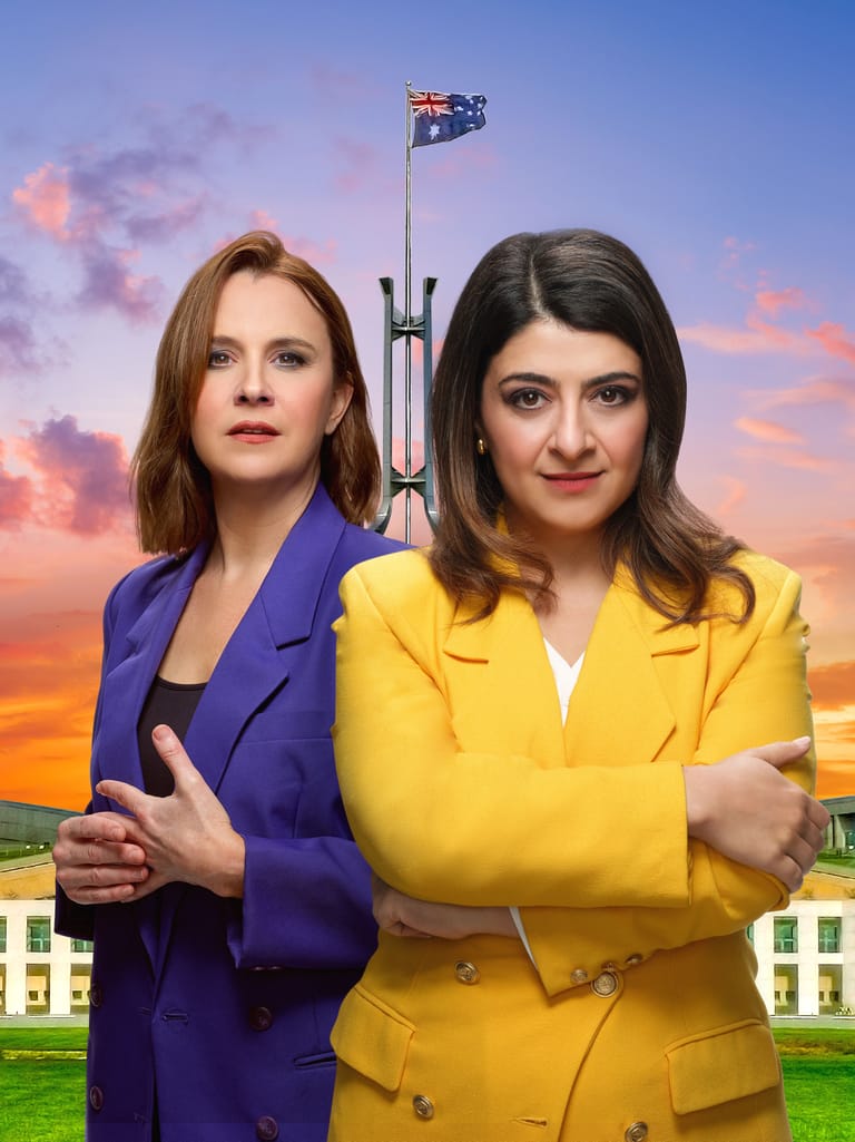 Two women in brightly coloured blazers stand before Parliament House with the Australian flag and sunset sky behind them.