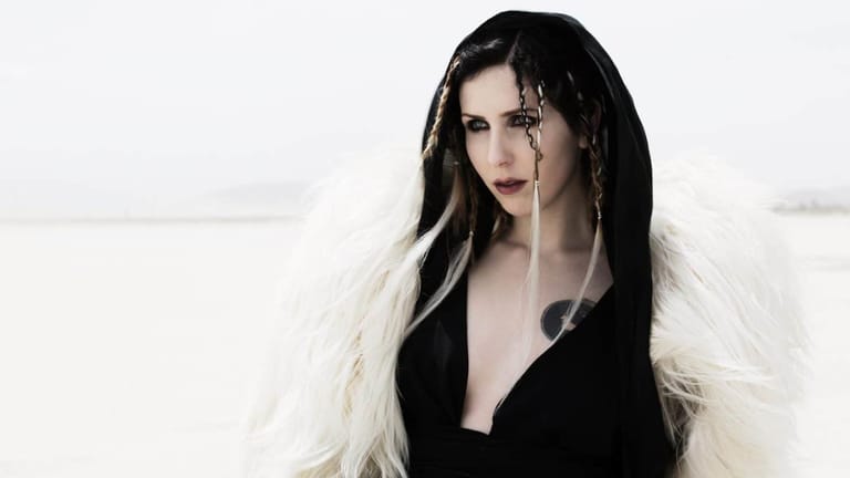 Person with long black and white streaked hair and dark lipstick against a white background.