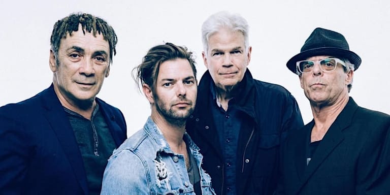 Four men in casual dark clothing pose together against a blue background.