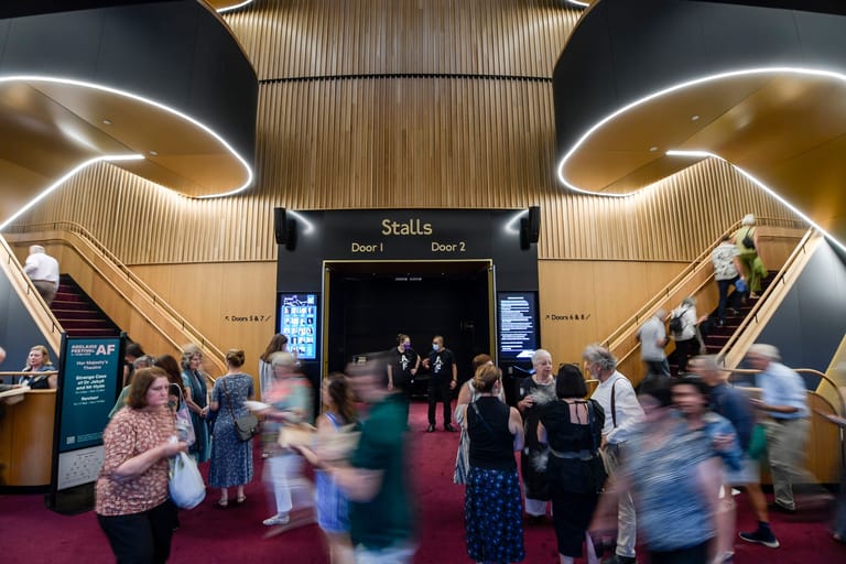 Foyer of a modern theatre with curved lighting and guests mingling on a red carpet beneath the Stalls entrance.