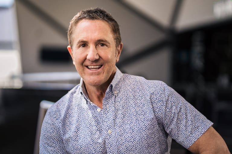Man in a blue patterned shirt smiling at the camera in an indoor studio setting.