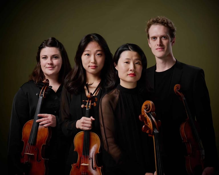 Four musicians in black clothing hold string instruments against a muted green background.