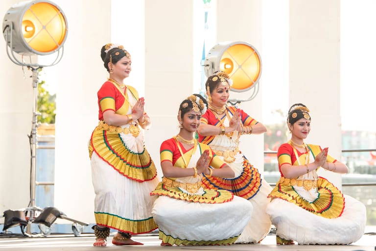 Young dancers in red and gold traditional costumes perform around a large white bowl during a cultural dance production.