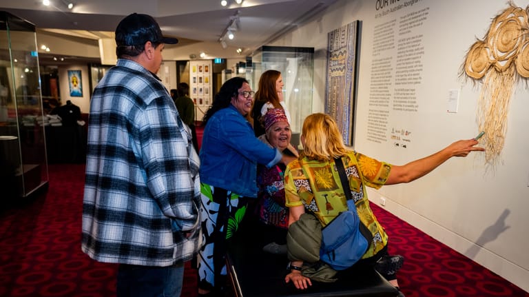 Museum visitors in casual clothing examine displays and artworks on walls and in glass cases.