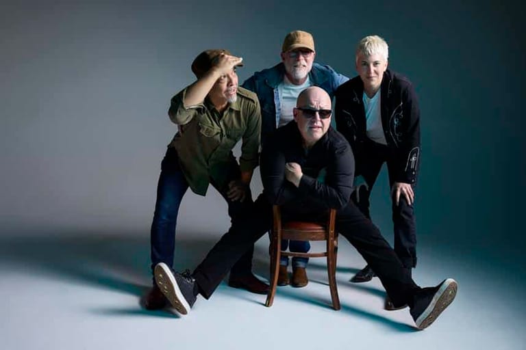 Four men in casual and smart-casual attire posed together against a teal gradient background.