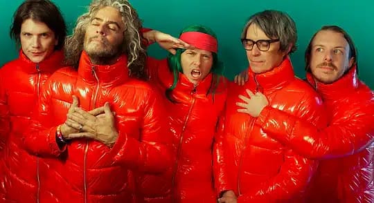 Five musicians in matching bright red puffy jackets pose together against a turquoise background.