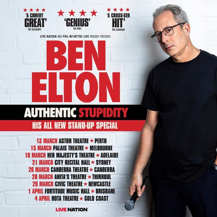 Man in glasses and black shirt stands beside promotional poster for stand-up comedy show tour.