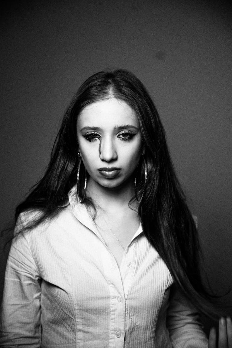 Black and white portrait of a young woman with long dark hair and silver hoop earrings, wearing a light-coloured shirt.