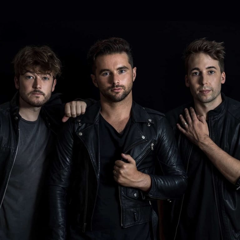 Three men in black leather jackets pose against a dark background.