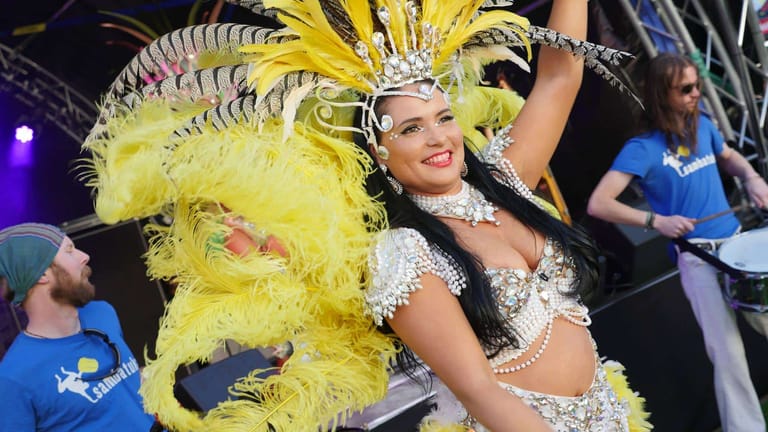 Performer in elaborate yellow feathered headdress and jewelled costume smiles during a carnival stage production.