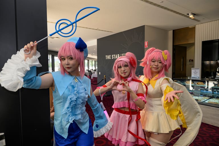 Three people in pink and blue wigs pose playfully in costume at an indoor event space.